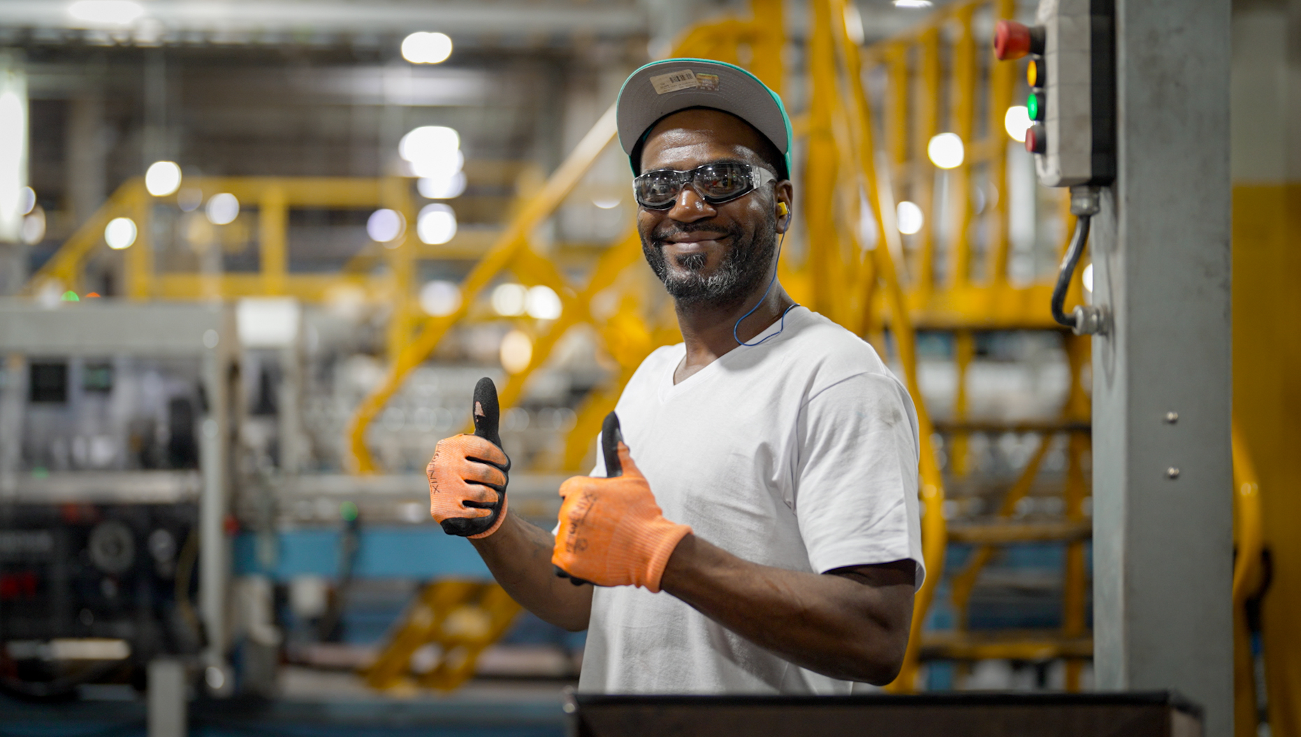 Smiling Anchor Glass employee in safety glasses and work gloves giving two thumbs up on the plant floor